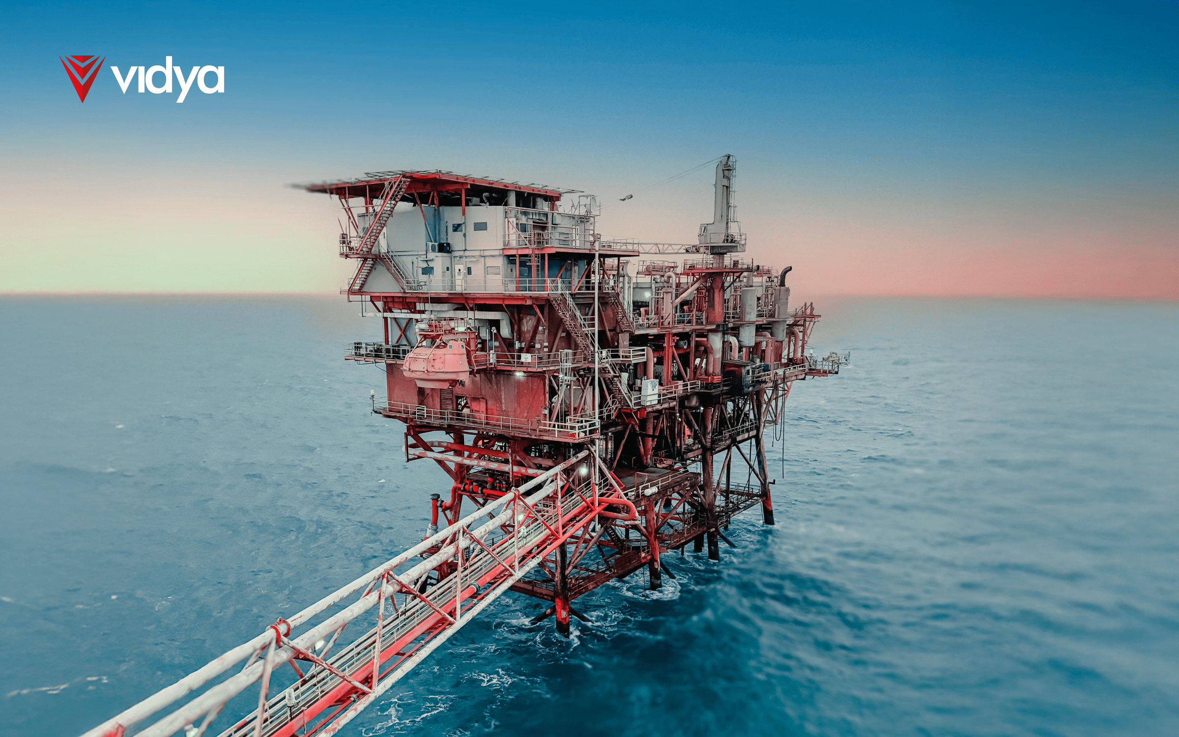 Offshore oil and gas platform standing in open sea at sunset, with visible structural details and a connected access bridge, branded with the Vidya logo.